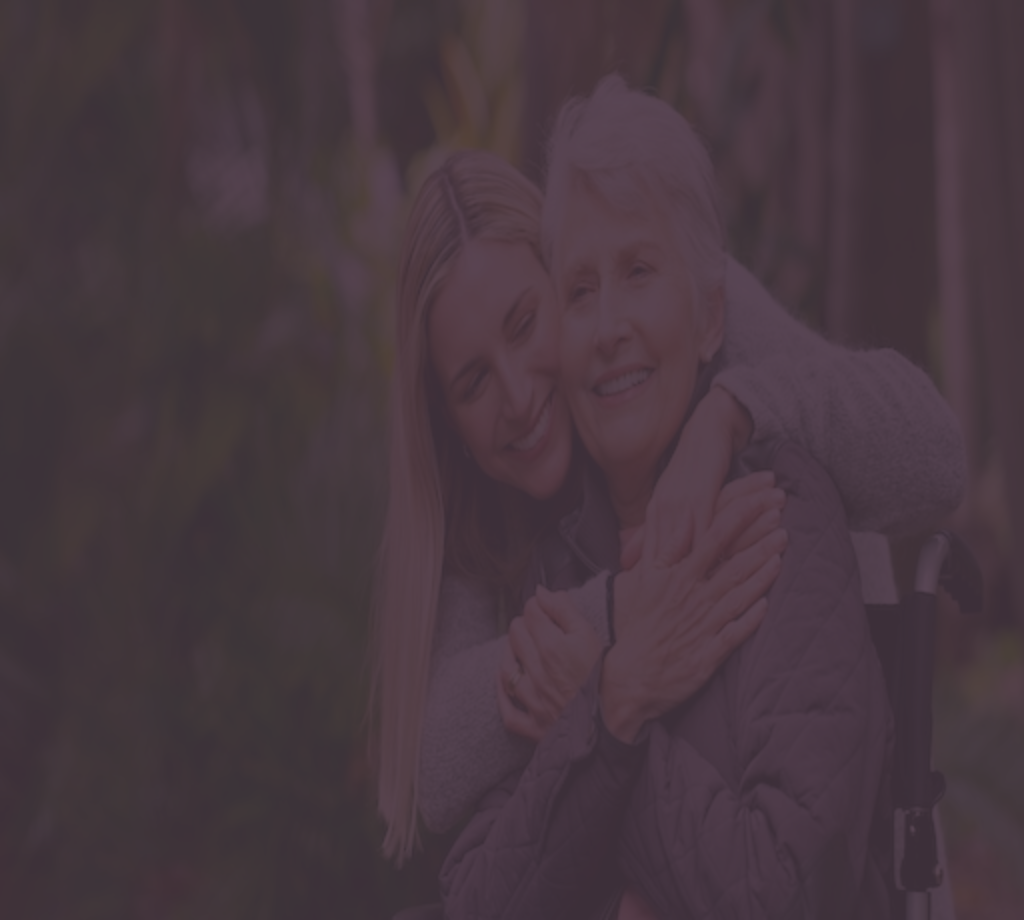 young woman hugging a woman in a wheelchair from behind