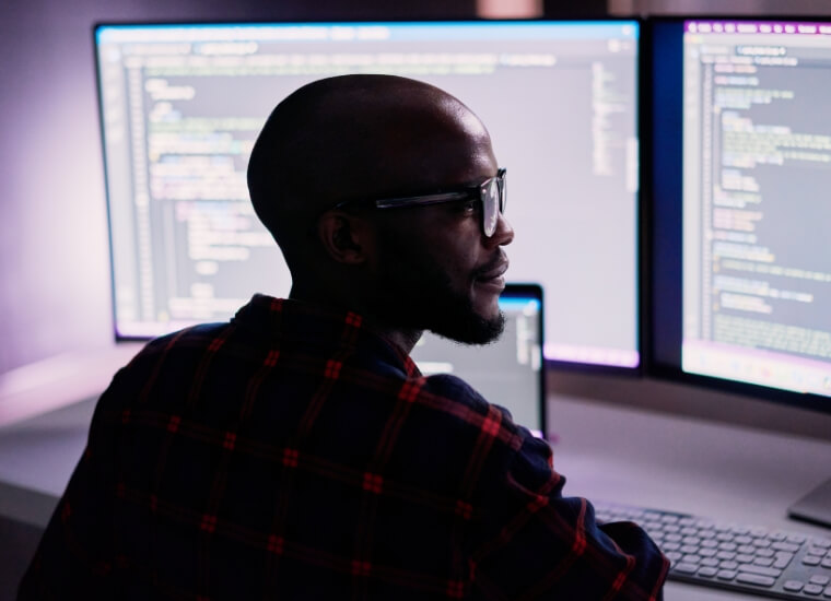 man writing code on two computer monitors